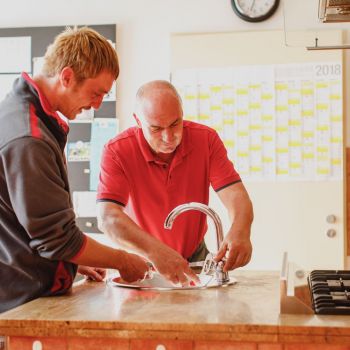Zwei Männer reparieren einen Wasserhahn in einer Küche.